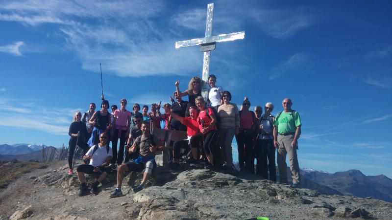 Eine Gruppe genießt den Ausblick an einem Gipfelkreuz